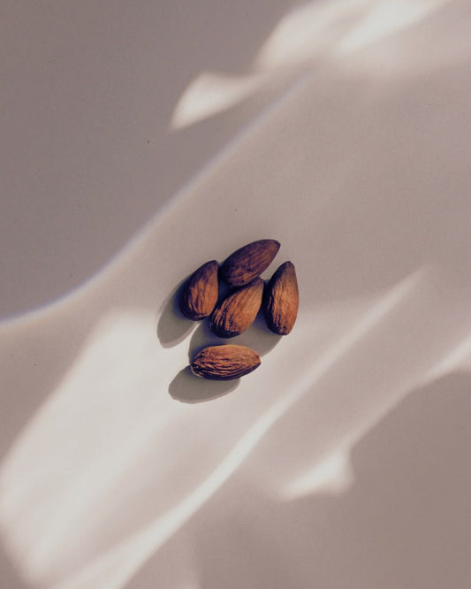 Warm toned brown almonds are presented on a mauve background with light reflections.
