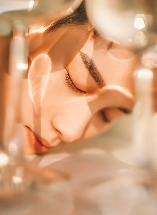 A beautiful Asian woman’s face with straight bold eyebrows and closed eyes is seen through an abstract glass frame