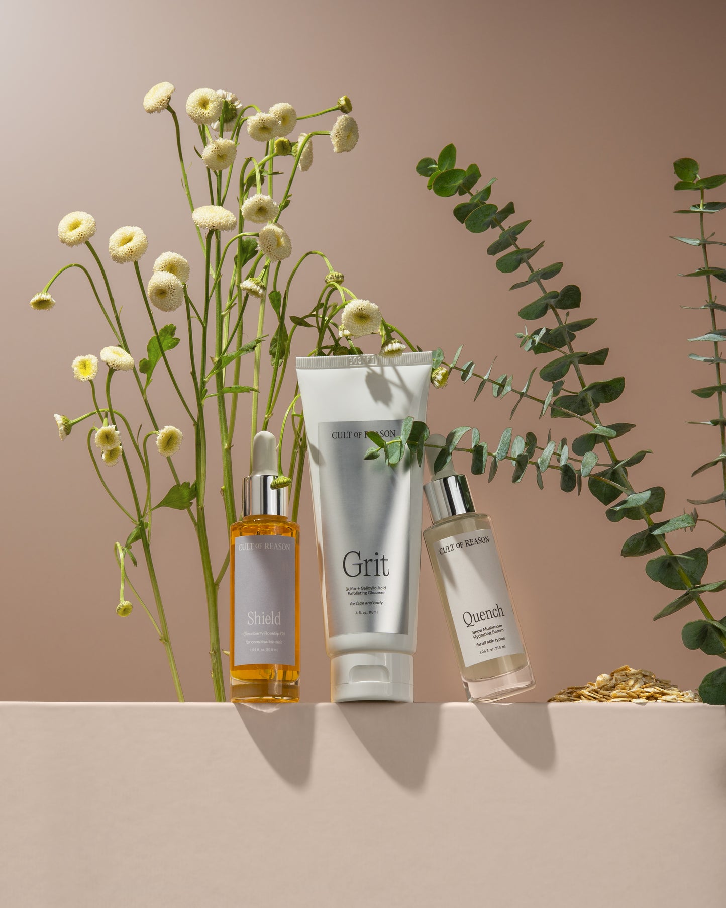 Group shot of Cult of Reason Skincare Grit Exfoliating Scrub, Quench Hydrating Serum, and Shield Bakuchiol Facial Oil on block with plants